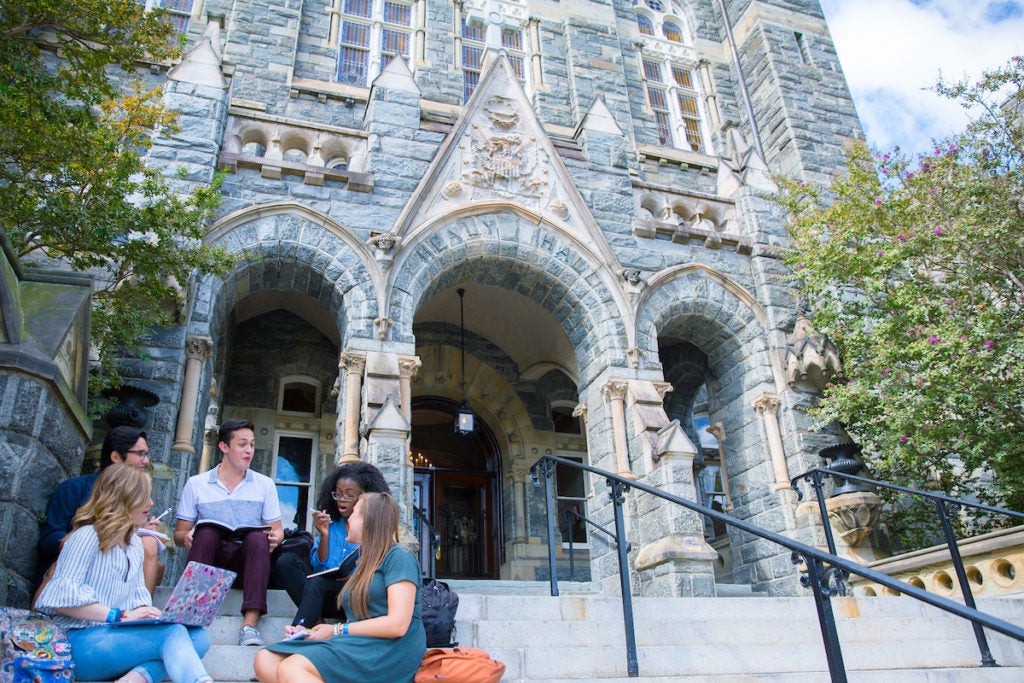 Students sitting on steps of a building on campus of Georgetown University