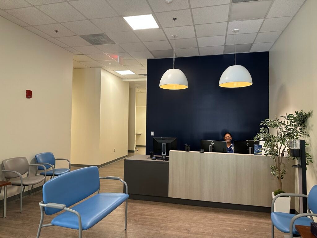 New waiting room in the entrance of the Student Health Center. Features chairs, a navy blue accent wall, and overhead lighting.