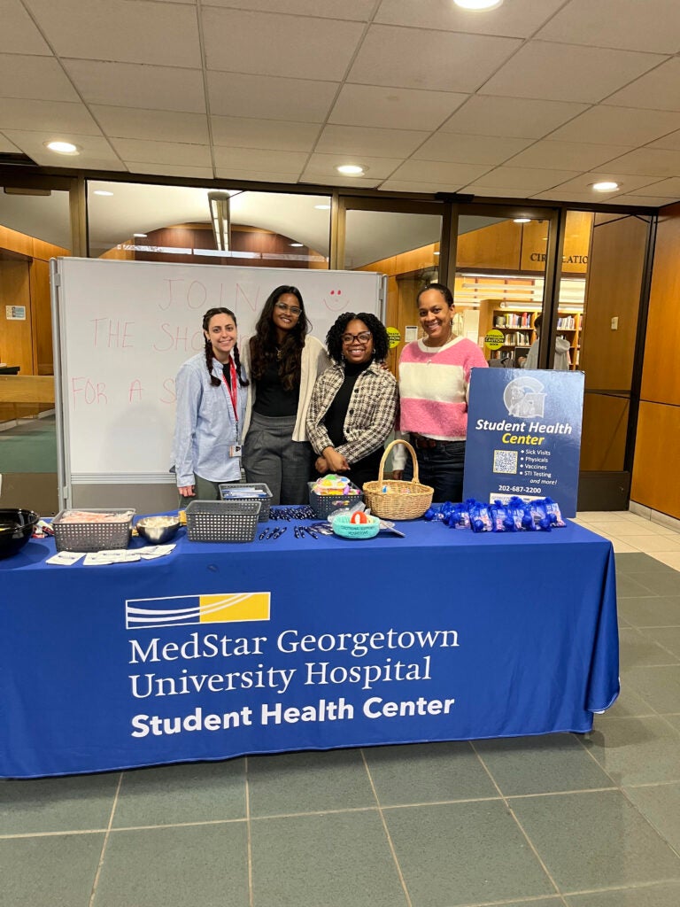 Student Health colleagues tabling in the Lau Library. Table features a blue Medstar Student Health Center tablecloth with free handouts for students.