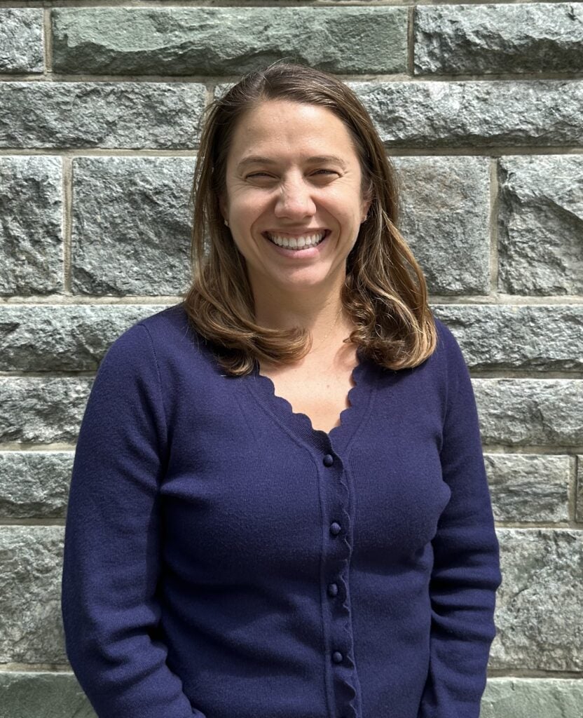 Smiling female with light brown hair, wearing a navy-blue button up sweater. 